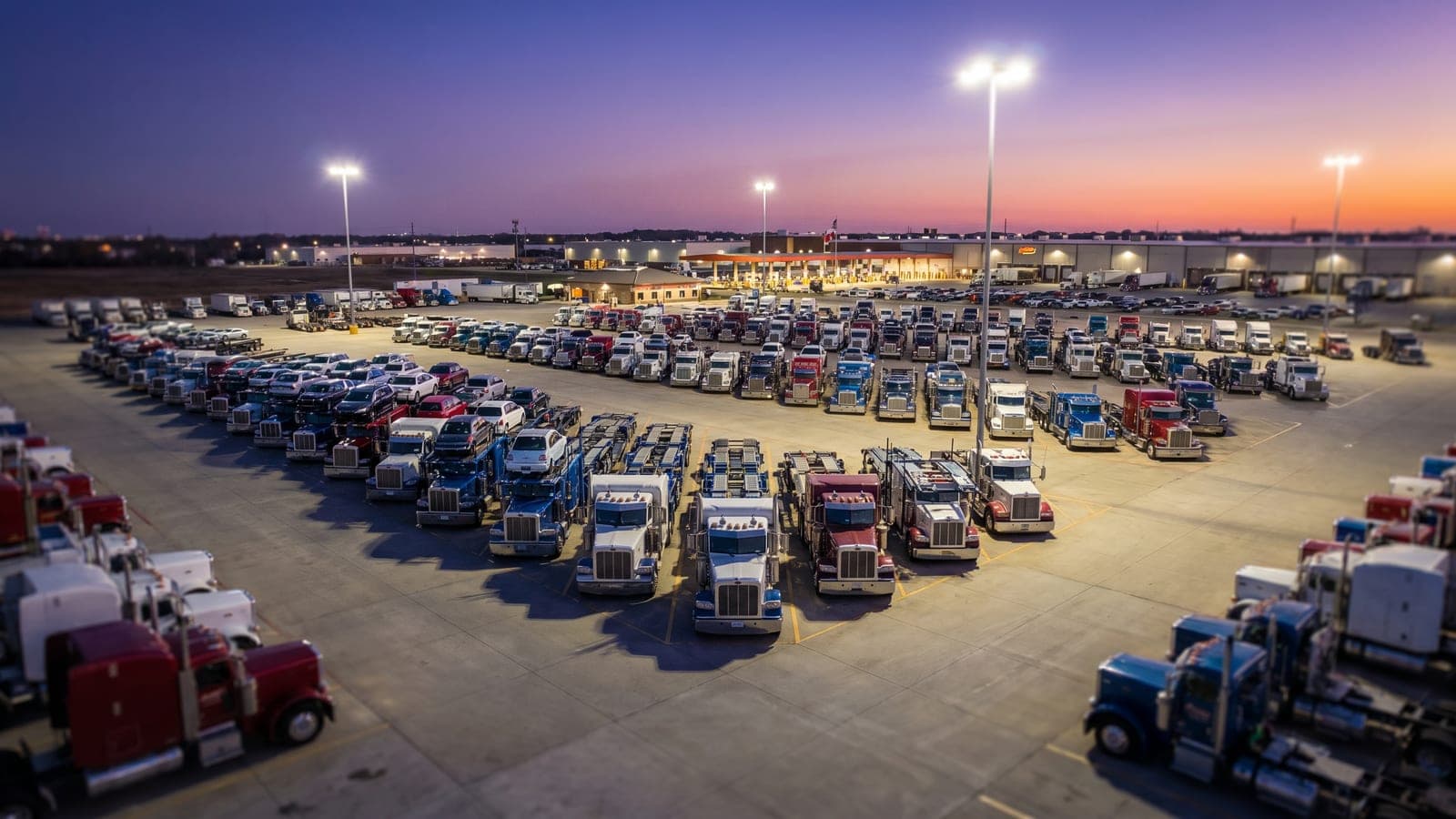 Shipity carrier-network fleet yard at dusk — long-haul trucks staged for departure